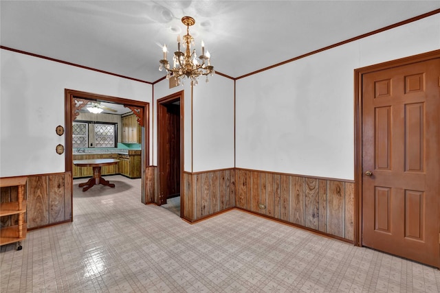 unfurnished room featuring an inviting chandelier, wood walls, wainscoting, and ornamental molding