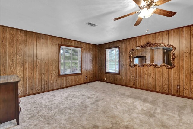 empty room with carpet floors, wood walls, a ceiling fan, and baseboards