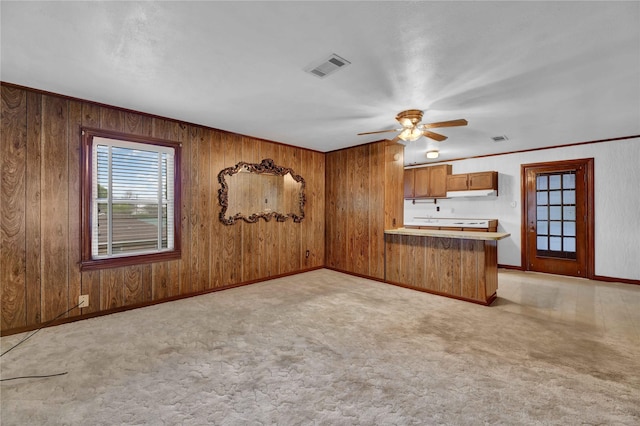 kitchen featuring brown cabinets, a peninsula, a ceiling fan, baseboards, and wooden walls