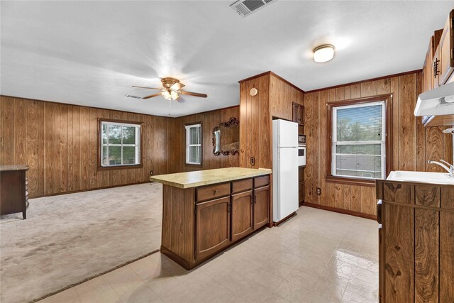 kitchen featuring plenty of natural light, wood walls, white appliances, a ceiling fan, and a peninsula