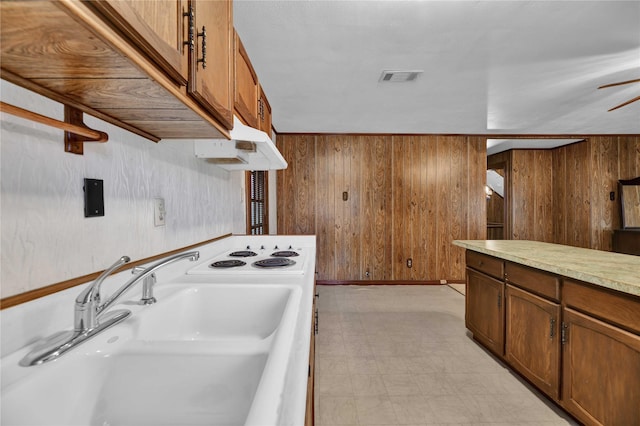 kitchen with a sink, wood walls, under cabinet range hood, light floors, and light countertops