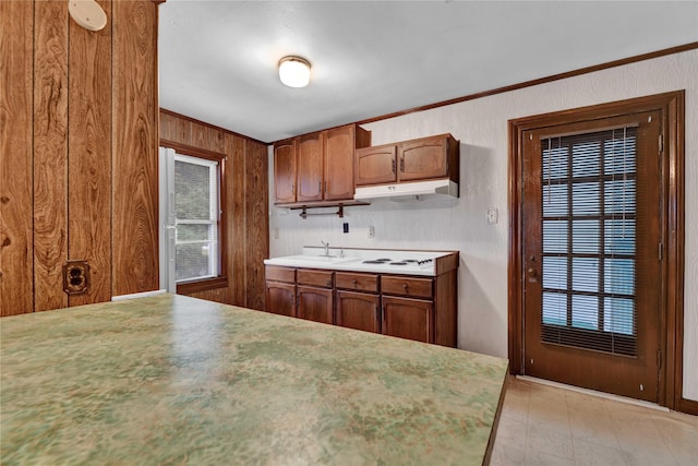 kitchen with under cabinet range hood, a sink, white stovetop, wood walls, and brown cabinets