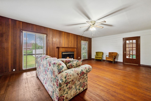 living room featuring wood walls, wood finished floors, ceiling fan, and a lit fireplace