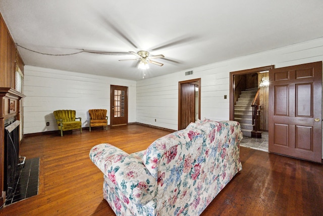 living room with visible vents, dark wood-style flooring, stairway, ceiling fan, and wooden walls