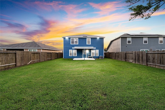 back house at dusk with central AC unit, a patio area, and a lawn