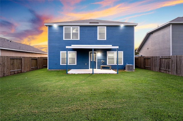 back house at dusk with central AC unit, a yard, and a patio area