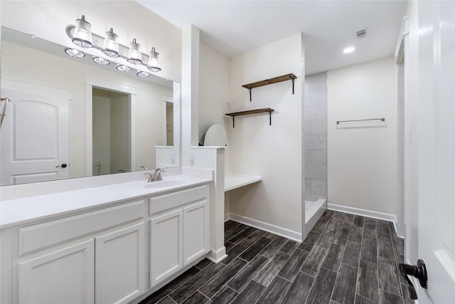 bathroom featuring vanity, a tile shower, and toilet