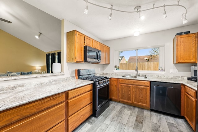 kitchen featuring sink, stainless steel range with gas stovetop, black dishwasher, light stone counters, and light wood-type flooring