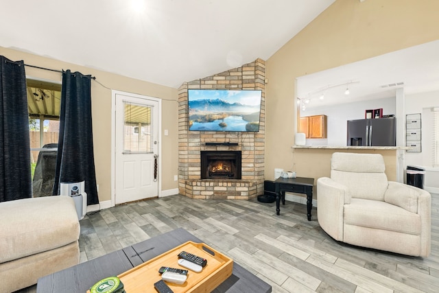 living room featuring vaulted ceiling, a brick fireplace, and light wood-type flooring