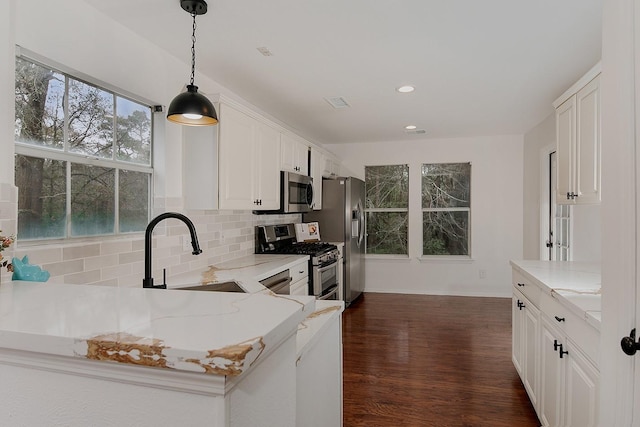 kitchen with sink, white cabinetry, appliances with stainless steel finishes, pendant lighting, and light stone countertops