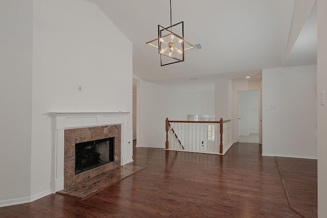 unfurnished living room featuring dark hardwood / wood-style flooring, a notable chandelier, and a tiled fireplace