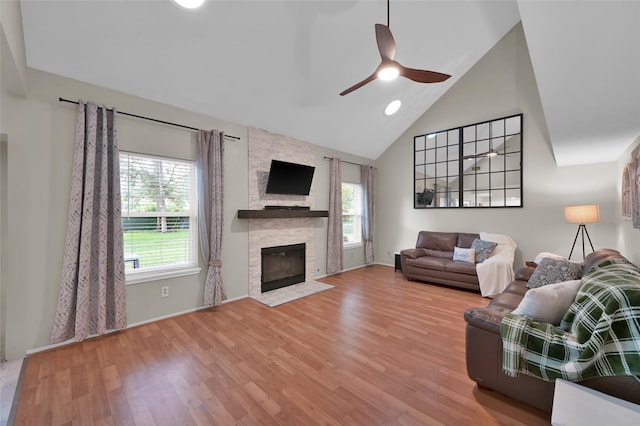 living room featuring wood-type flooring, a stone fireplace, ceiling fan, and high vaulted ceiling