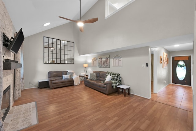 living room featuring high vaulted ceiling, a stone fireplace, hardwood / wood-style floors, and ceiling fan