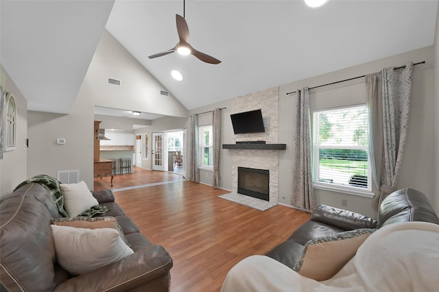 living room with ceiling fan, high vaulted ceiling, a fireplace, and light hardwood / wood-style floors