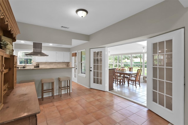 kitchen featuring tasteful backsplash, island range hood, white cabinets, light tile patterned flooring, and kitchen peninsula