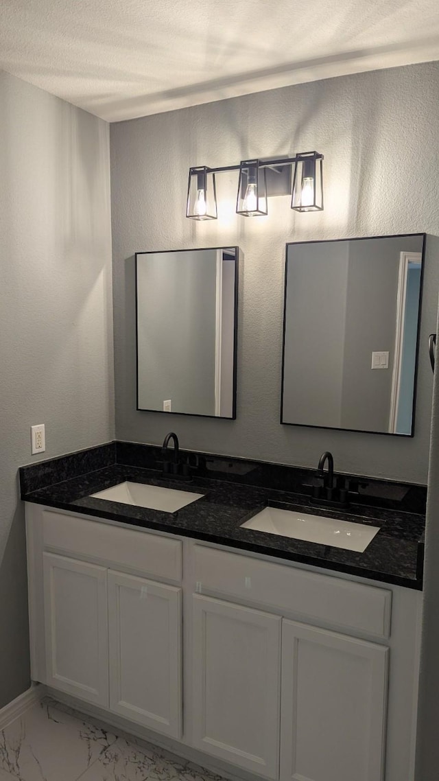 bathroom featuring marble finish floor, a sink, a textured ceiling, and double vanity