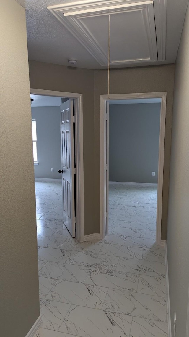 hallway with marble finish floor, attic access, and baseboards