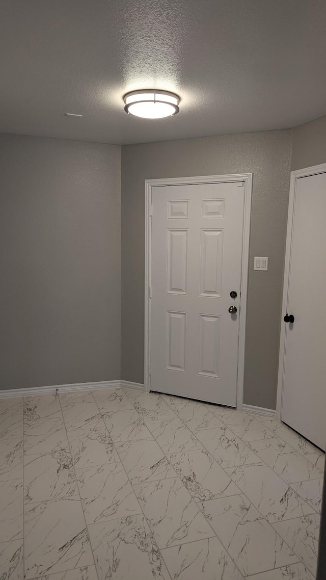 entrance foyer with marble finish floor, baseboards, and a textured ceiling