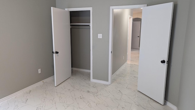 unfurnished bedroom with marble finish floor, baseboards, and a closet