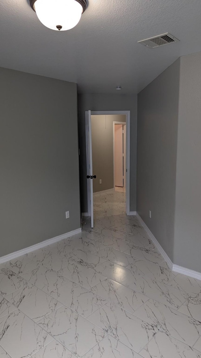 unfurnished room with marble finish floor, visible vents, a textured ceiling, and baseboards