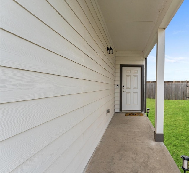 entrance to property featuring fence, a patio, and a lawn