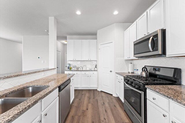 kitchen with white cabinets, decorative backsplash, wood finished floors, stainless steel appliances, and stone counters