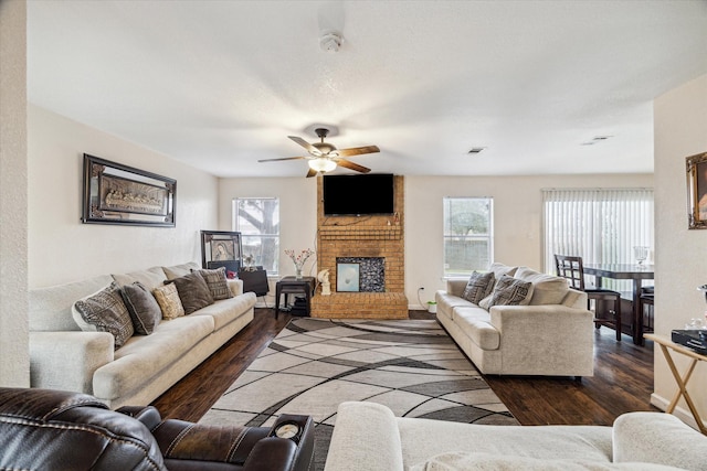 living area featuring a brick fireplace, visible vents, a ceiling fan, and dark wood-style flooring