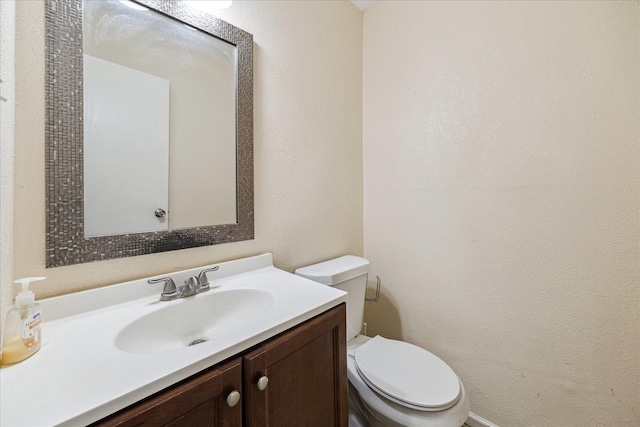 half bathroom with toilet, a textured wall, and vanity