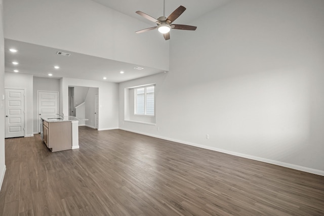 unfurnished living room with dark wood finished floors, visible vents, a sink, ceiling fan, and baseboards