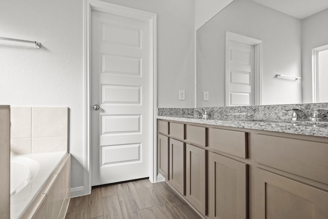 bathroom with tiled tub, wood finished floors, a sink, and double vanity