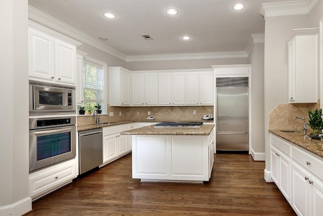 kitchen featuring sink, light stone counters, built in appliances, a center island, and white cabinets