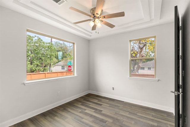 empty room with dark wood-type flooring, ceiling fan, plenty of natural light, and a raised ceiling