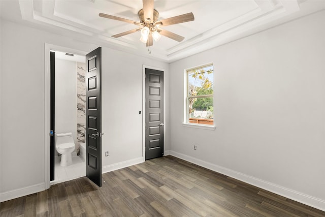 unfurnished bedroom with a raised ceiling, dark wood-type flooring, connected bathroom, and ceiling fan