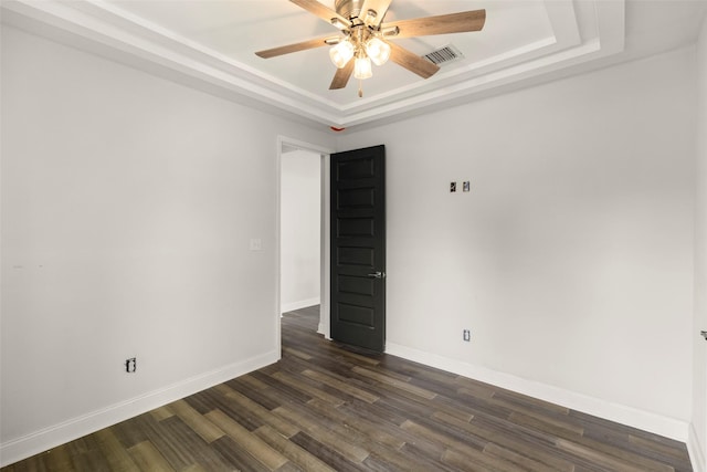 empty room with a tray ceiling, dark wood-type flooring, and ceiling fan