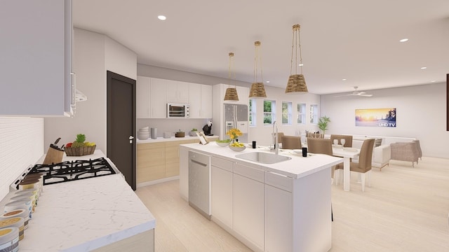 kitchen featuring white cabinetry, sink, hanging light fixtures, a center island with sink, and light hardwood / wood-style flooring