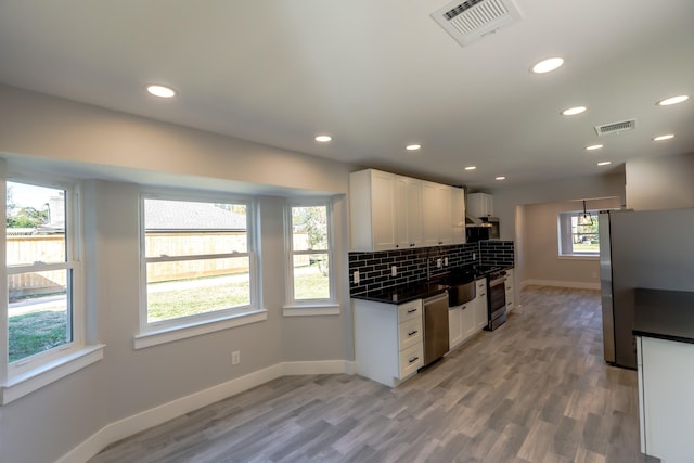 kitchen with appliances with stainless steel finishes, light wood-type flooring, white cabinets, and backsplash