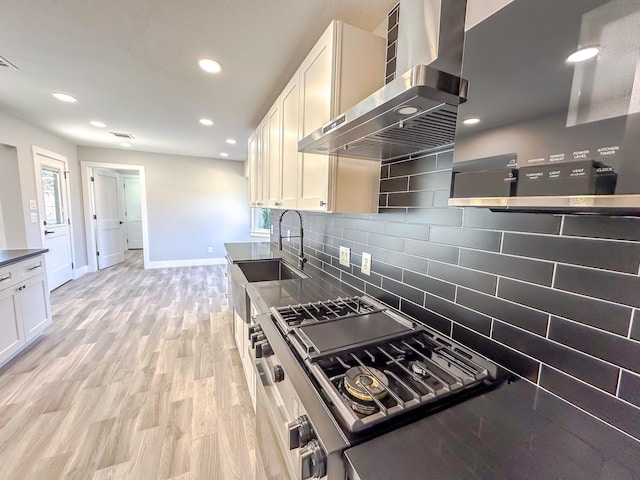 kitchen featuring stainless steel gas stove, range hood, white cabinetry, sink, and light hardwood / wood-style flooring