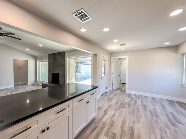 kitchen with lofted ceiling, a brick fireplace, ceiling fan, light hardwood / wood-style floors, and white cabinets