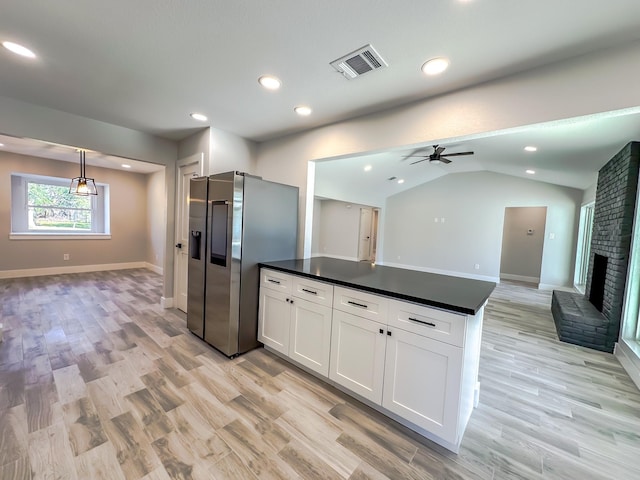 kitchen featuring vaulted ceiling, stainless steel fridge, white cabinets, hanging light fixtures, and a brick fireplace