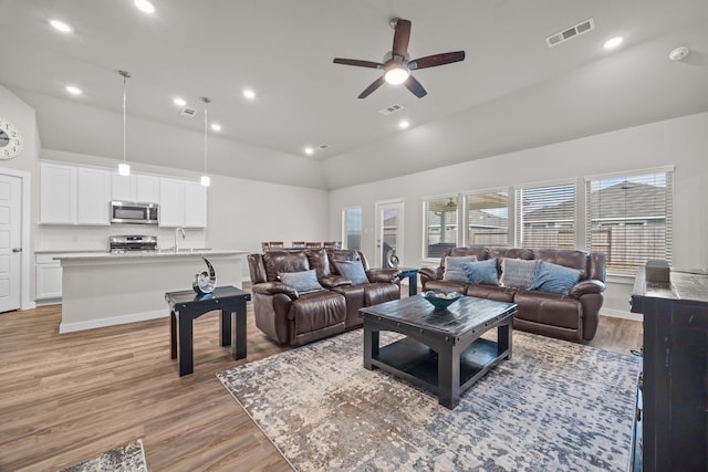 living room with ceiling fan, sink, vaulted ceiling, and light hardwood / wood-style flooring