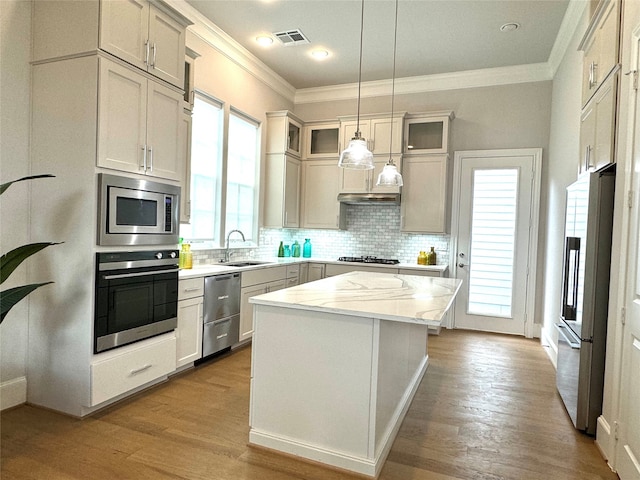 kitchen featuring sink, appliances with stainless steel finishes, a center island, light stone counters, and decorative light fixtures