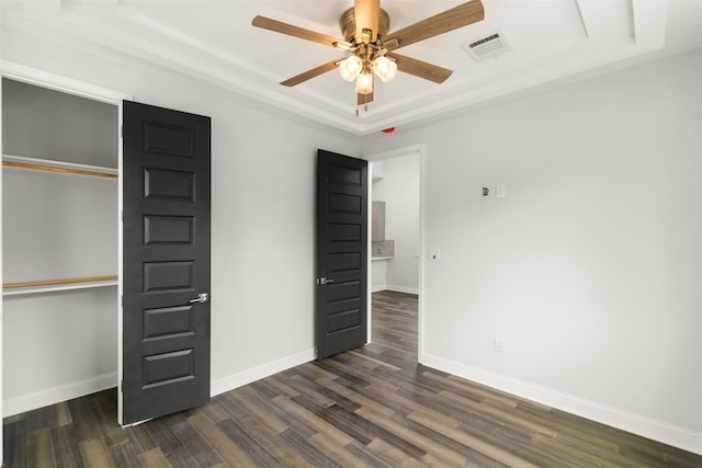 unfurnished bedroom with dark hardwood / wood-style flooring, a tray ceiling, a closet, and ceiling fan