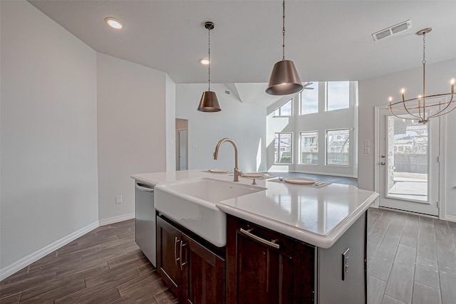 kitchen featuring stainless steel dishwasher, decorative light fixtures, sink, and a center island with sink