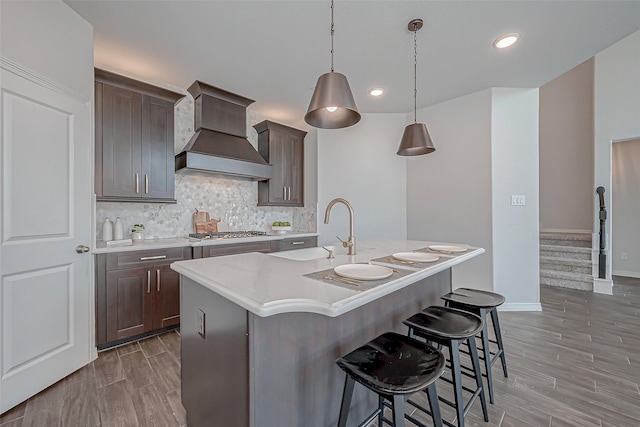 kitchen with premium range hood, pendant lighting, stainless steel gas stovetop, decorative backsplash, and a kitchen island with sink