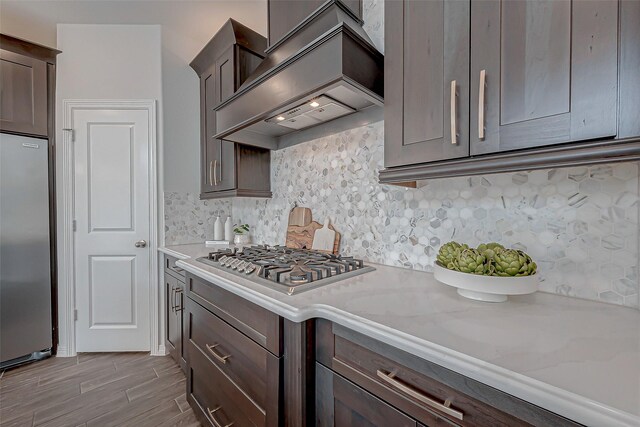 kitchen with light stone counters, decorative backsplash, custom range hood, and appliances with stainless steel finishes