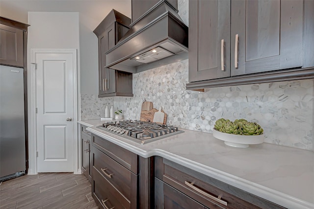 8934 Stanley Oak Dr, Missouri City, TX 77459 - kitchen with stainless steel appliances, premium range hood, dark brown cabinetry, and decorative backsplash