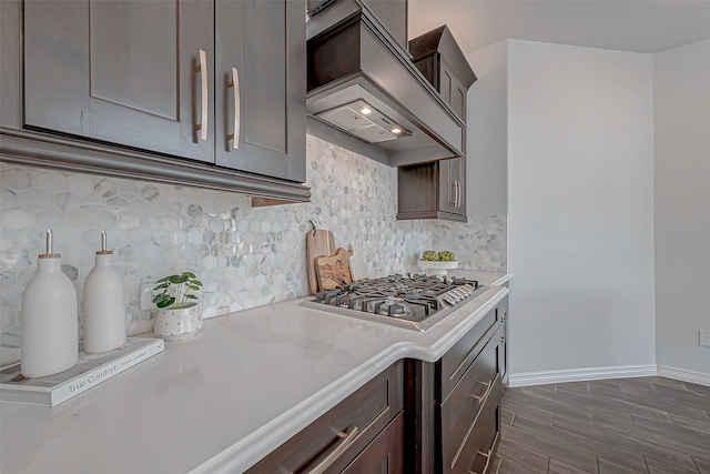 kitchen with light stone counters, custom exhaust hood, dark hardwood / wood-style flooring, stainless steel gas cooktop, and decorative backsplash