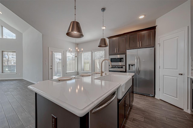 kitchen featuring an island with sink, stainless steel appliances, decorative light fixtures, sink, and dark brown cabinets