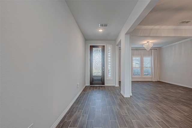 entryway with dark wood-type flooring, crown molding, and an inviting chandelier