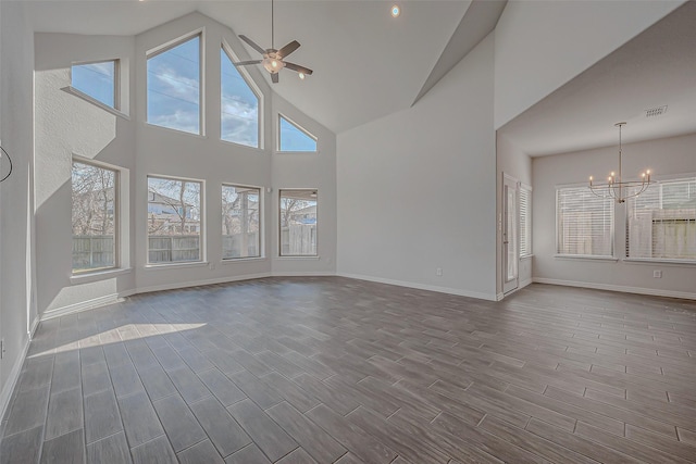 unfurnished living room featuring high vaulted ceiling, a healthy amount of sunlight, and ceiling fan with notable chandelier